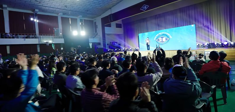 어두운 강당에서 무대를 바라보며 박수를 치는 관객들