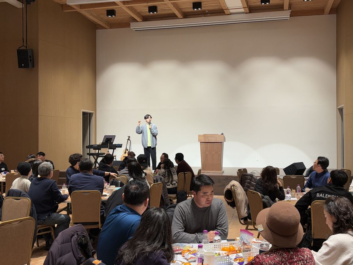 무대 앞에서 진행자가 규칙을 설명하고 참가자들이 테이블에 앉아 듣는 모습