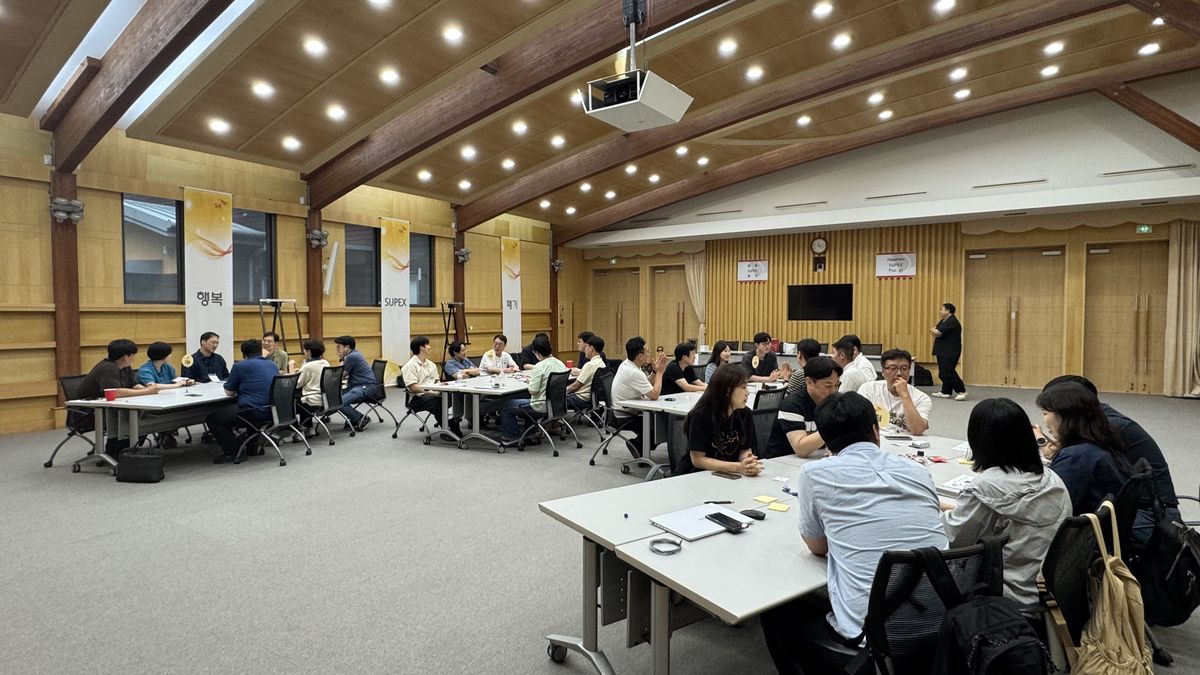 연수원 강당에서 팀별 테이블에 모여 창의 미션을 수행하는 참가자들